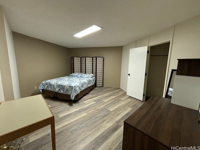 bedroom with a spacious closet, a closet, light hardwood / wood-style floors, and a textured ceiling