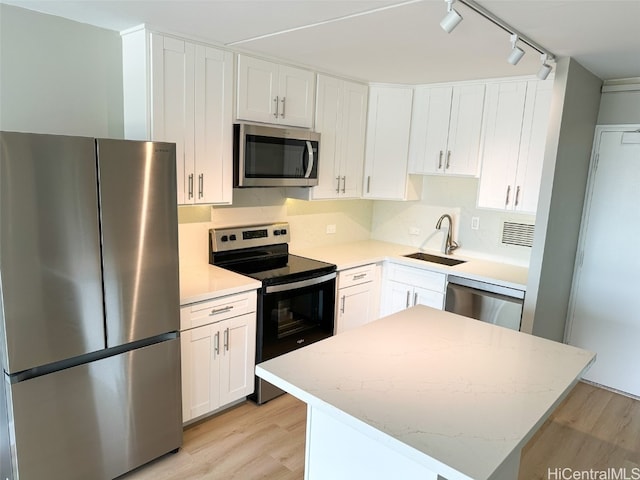 kitchen with white cabinets, stainless steel appliances, sink, light hardwood / wood-style floors, and a center island