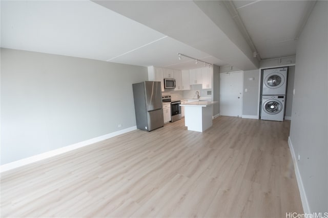 unfurnished living room with light hardwood / wood-style flooring, stacked washer / drying machine, sink, and track lighting