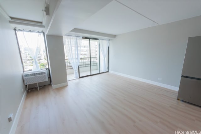 unfurnished living room with cooling unit, a wealth of natural light, and light wood-type flooring