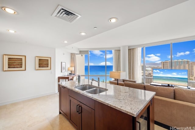 kitchen with light stone counters, sink, a wealth of natural light, and an island with sink