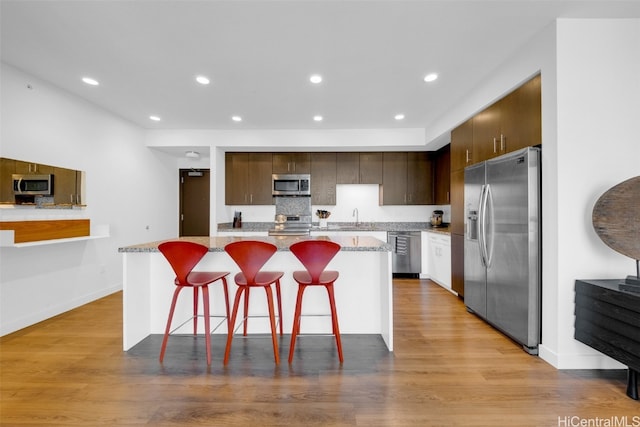 kitchen with sink, a breakfast bar, a center island, light wood-type flooring, and appliances with stainless steel finishes