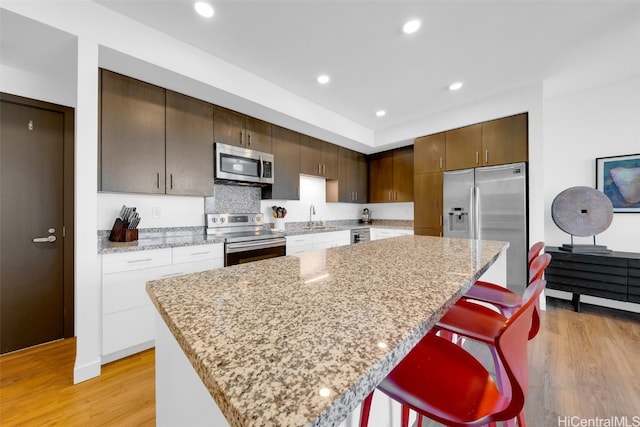 kitchen with stainless steel appliances, light wood-type flooring, a kitchen island, and a kitchen breakfast bar