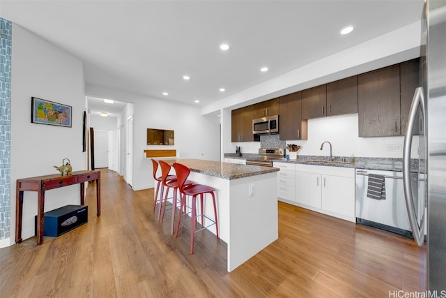 kitchen featuring light hardwood / wood-style flooring, dark brown cabinets, stainless steel appliances, a center island, and white cabinets