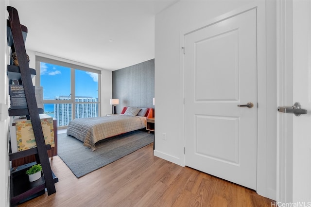 bedroom with light hardwood / wood-style floors, a wall of windows, and a water view