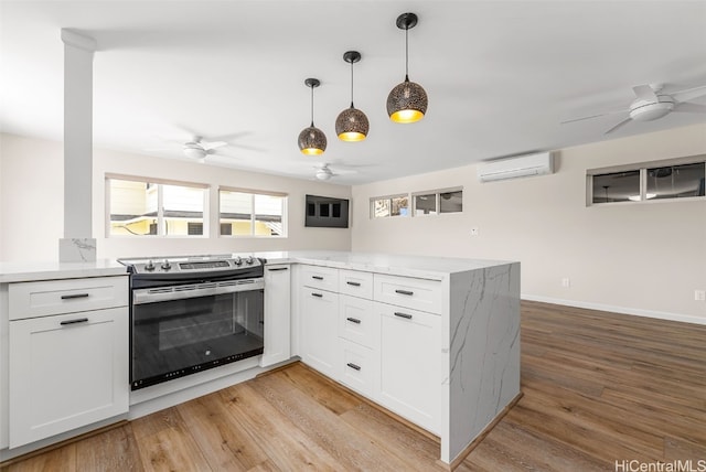 kitchen with stainless steel range with electric cooktop, kitchen peninsula, a wall mounted AC, white cabinets, and light wood-type flooring