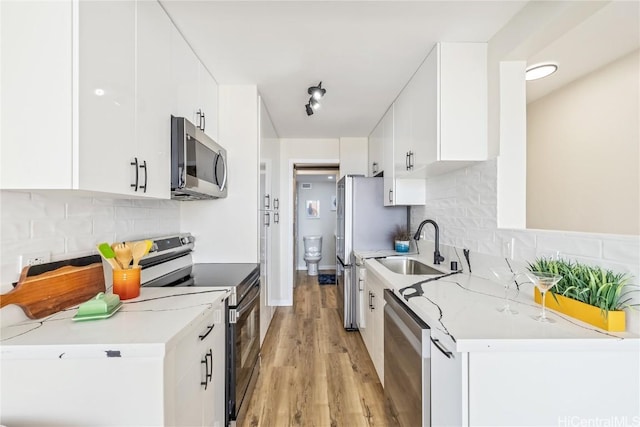 kitchen with sink, stainless steel appliances, tasteful backsplash, white cabinets, and light wood-type flooring