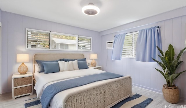 bedroom featuring an AC wall unit, light hardwood / wood-style flooring, and multiple windows