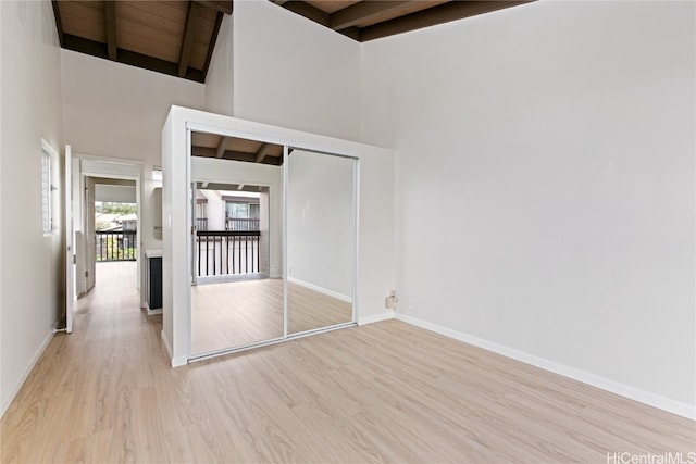 interior space with beamed ceiling, a high ceiling, and light wood-type flooring