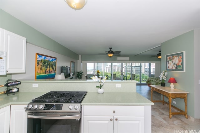 kitchen with an AC wall unit, kitchen peninsula, ceiling fan, white cabinets, and gas range