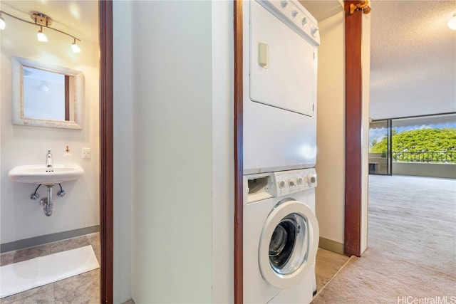 laundry area with light colored carpet, stacked washer and clothes dryer, sink, and a textured ceiling