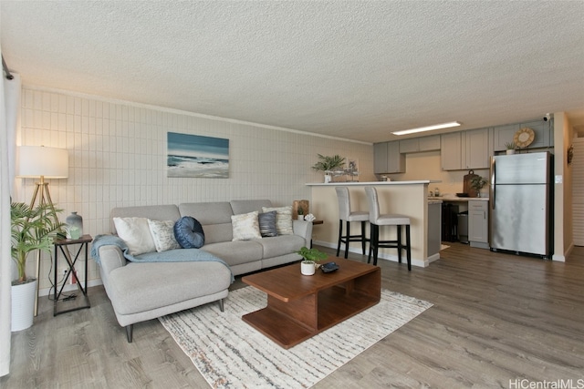 living room featuring tile walls, crown molding, light hardwood / wood-style flooring, and a textured ceiling