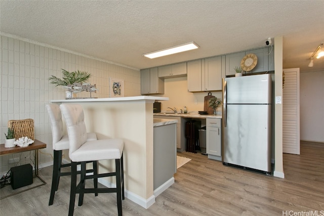 kitchen featuring a kitchen bar, tile walls, gray cabinets, stainless steel refrigerator, and light hardwood / wood-style flooring