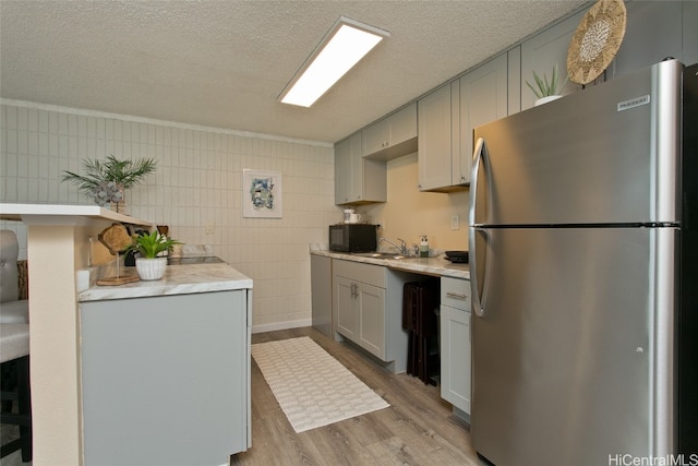 kitchen featuring sink, a textured ceiling, light hardwood / wood-style floors, crown molding, and stainless steel refrigerator