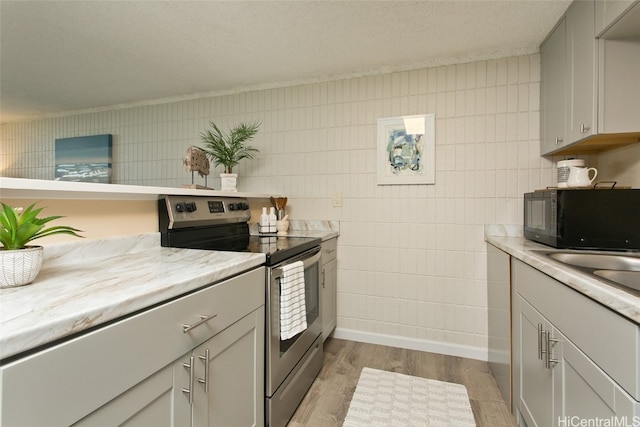 kitchen featuring a textured ceiling, light stone countertops, tile walls, light wood-type flooring, and stainless steel range with electric stovetop