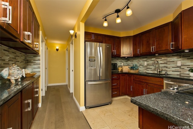 kitchen featuring backsplash, track lighting, sink, stainless steel refrigerator with ice dispenser, and dark stone countertops