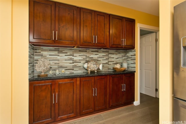 bar with backsplash, dark stone countertops, stainless steel fridge, and dark wood-type flooring