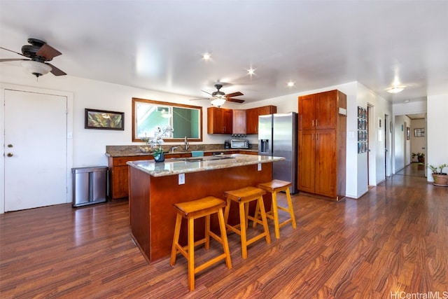 kitchen featuring stainless steel fridge, dark hardwood / wood-style flooring, light stone countertops, and a kitchen island