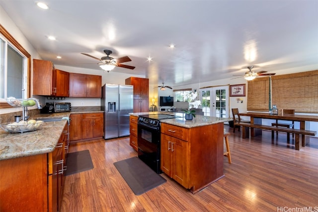 kitchen with a kitchen breakfast bar, black electric range oven, stainless steel refrigerator with ice dispenser, hardwood / wood-style floors, and a kitchen island