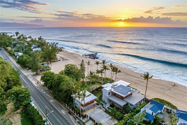 aerial view at dusk featuring a water view and a beach view