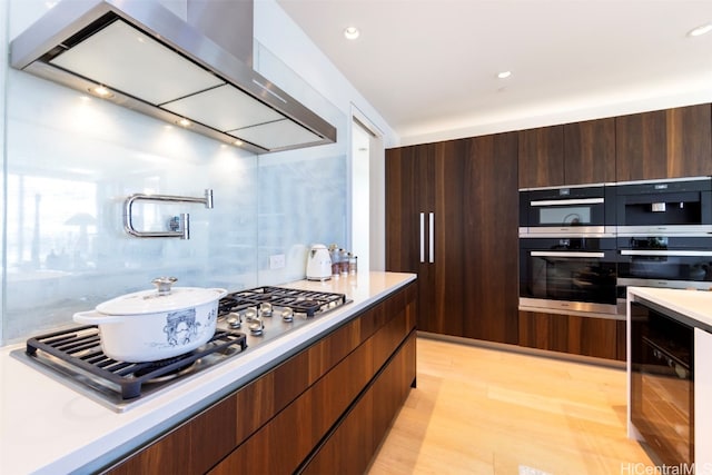 kitchen featuring appliances with stainless steel finishes, wall chimney exhaust hood, and light hardwood / wood-style flooring