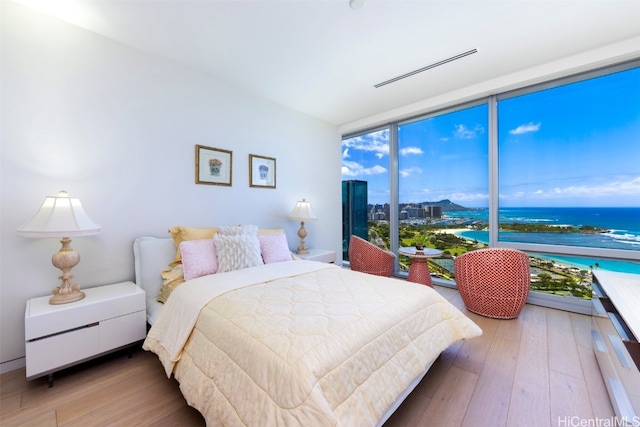 bedroom with a water view, hardwood / wood-style flooring, and a wall of windows