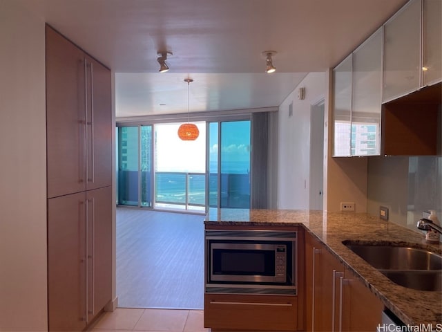 kitchen with stainless steel microwave, sink, light stone countertops, light tile patterned flooring, and decorative light fixtures