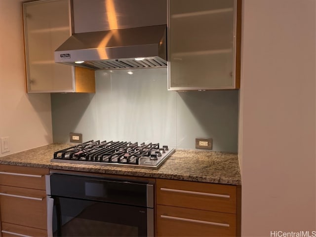 kitchen with stainless steel gas cooktop, wall chimney exhaust hood, oven, and stone countertops