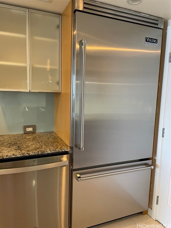 kitchen featuring appliances with stainless steel finishes, light tile patterned flooring, and dark stone counters