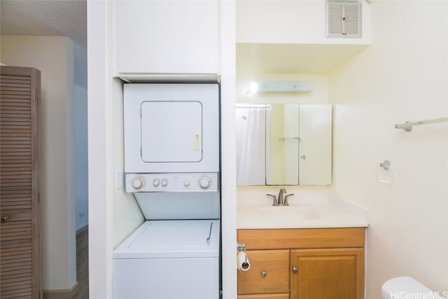 clothes washing area featuring a textured ceiling, stacked washer / dryer, and sink