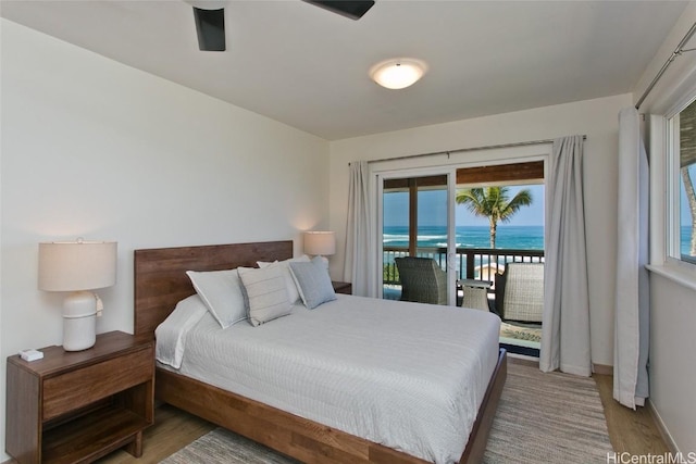 bedroom with access to exterior, wood-type flooring, a water view, and multiple windows