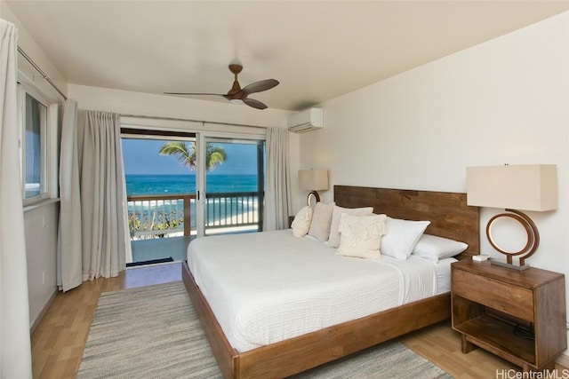 bedroom featuring access to outside, a water view, light hardwood / wood-style flooring, ceiling fan, and a wall unit AC