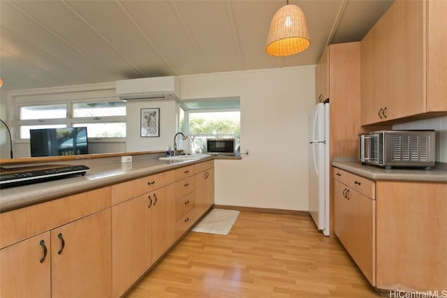 kitchen with light brown cabinetry, a wall unit AC, sink, light hardwood / wood-style flooring, and hanging light fixtures