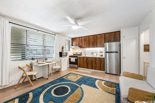 kitchen featuring decorative backsplash, exhaust hood, ceiling fan, appliances with stainless steel finishes, and light wood-type flooring