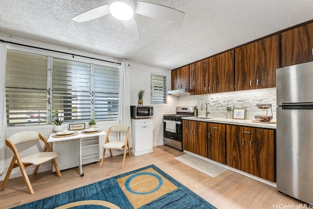 kitchen featuring decorative backsplash, a textured ceiling, light wood-type flooring, sink, and stainless steel appliances