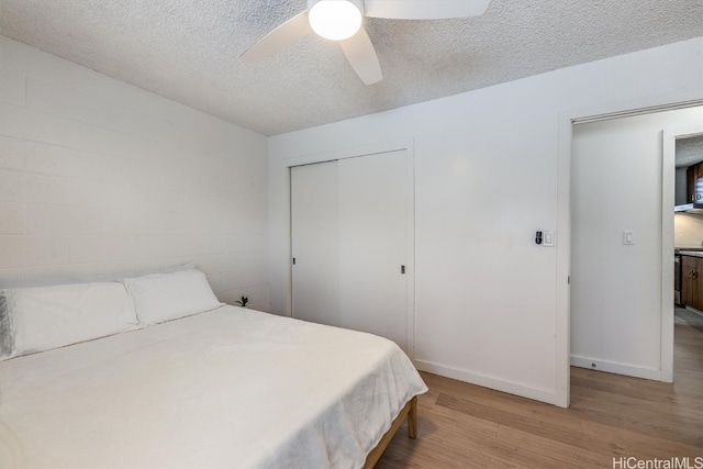 bedroom featuring light hardwood / wood-style flooring, a textured ceiling, a closet, and ceiling fan