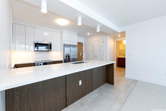 kitchen with a sink, light countertops, stainless steel appliances, white cabinetry, and modern cabinets