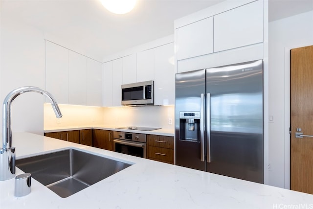 kitchen featuring white cabinetry, appliances with stainless steel finishes, sink, and light stone counters