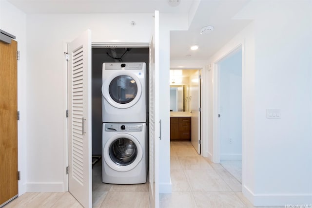 laundry room featuring stacked washing maching and dryer, baseboards, light tile patterned floors, and laundry area