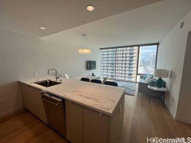 kitchen with a sink, a peninsula, light countertops, dishwasher, and wood finished floors