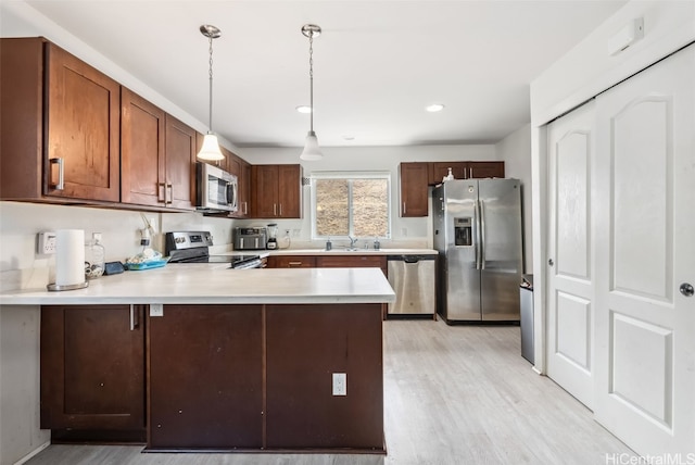 kitchen featuring decorative light fixtures, sink, light hardwood / wood-style floors, kitchen peninsula, and stainless steel appliances