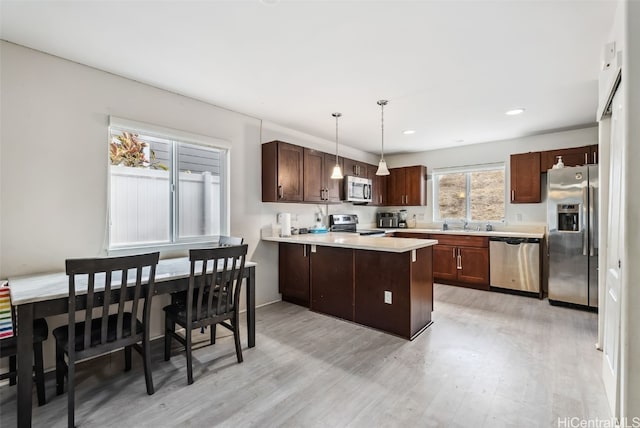 kitchen with appliances with stainless steel finishes, decorative light fixtures, kitchen peninsula, dark brown cabinets, and light hardwood / wood-style flooring