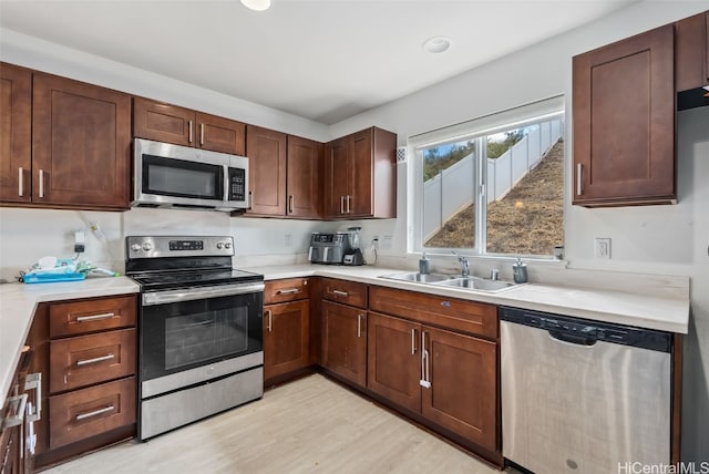 kitchen with appliances with stainless steel finishes, sink, and light wood-type flooring