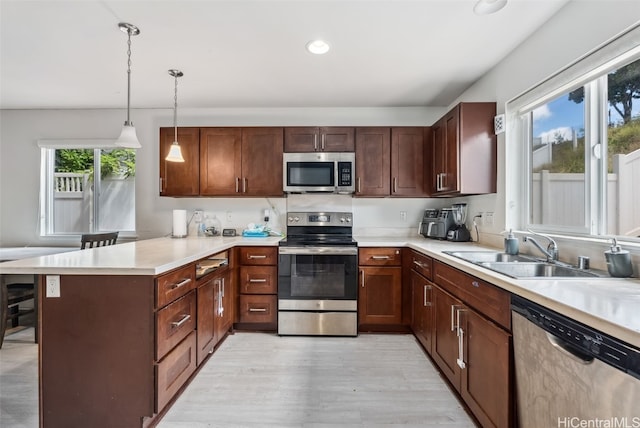 kitchen featuring sink, light hardwood / wood-style flooring, kitchen peninsula, pendant lighting, and stainless steel appliances