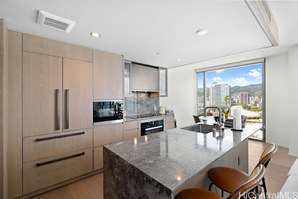 kitchen with stone counters, black appliances, a center island with sink, and a breakfast bar area