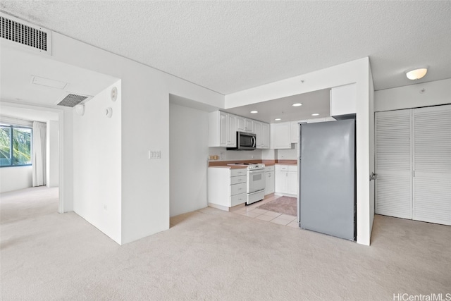 kitchen with appliances with stainless steel finishes, white cabinetry, light colored carpet, and a textured ceiling