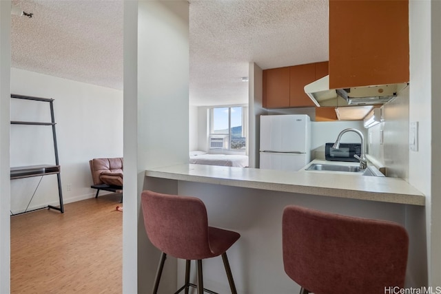 kitchen with kitchen peninsula, a breakfast bar area, a textured ceiling, light hardwood / wood-style floors, and white fridge