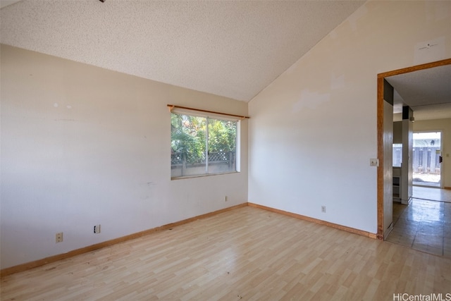 spare room featuring vaulted ceiling, a textured ceiling, and light wood-type flooring