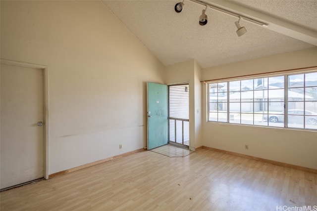 empty room with light hardwood / wood-style flooring, a textured ceiling, track lighting, and vaulted ceiling