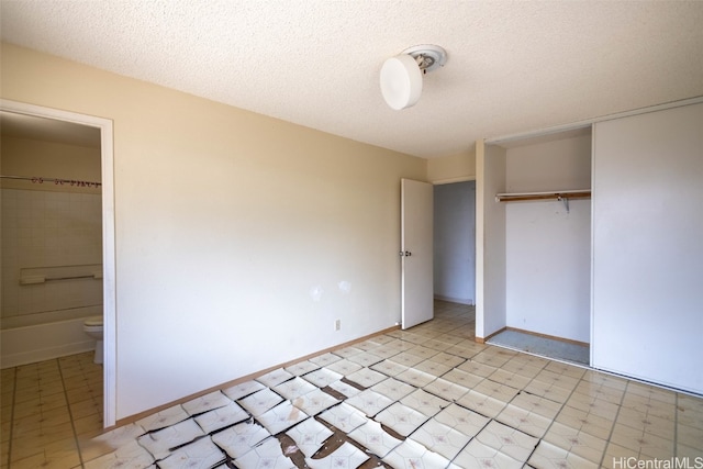 unfurnished bedroom with a closet, a textured ceiling, and ensuite bath